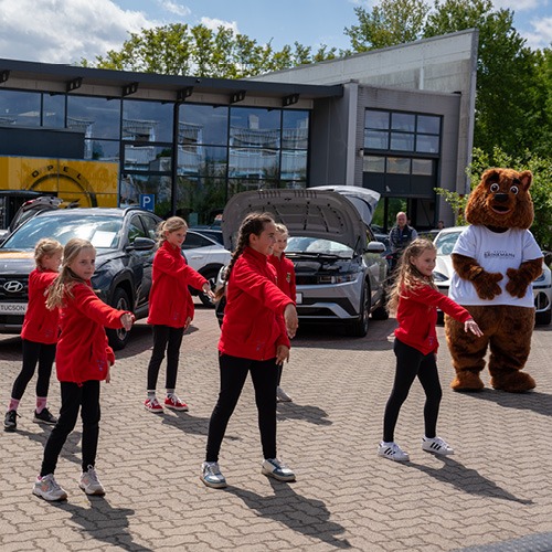 kinder in orangen Sachen und ein brauner Bär, die was zeigen